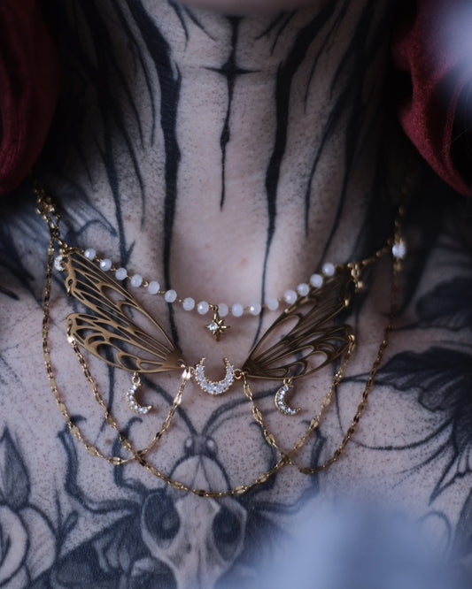 Collier Nova doré avec ailes ajourées, croissants de lune, étoile centrale et chaînes délicates.