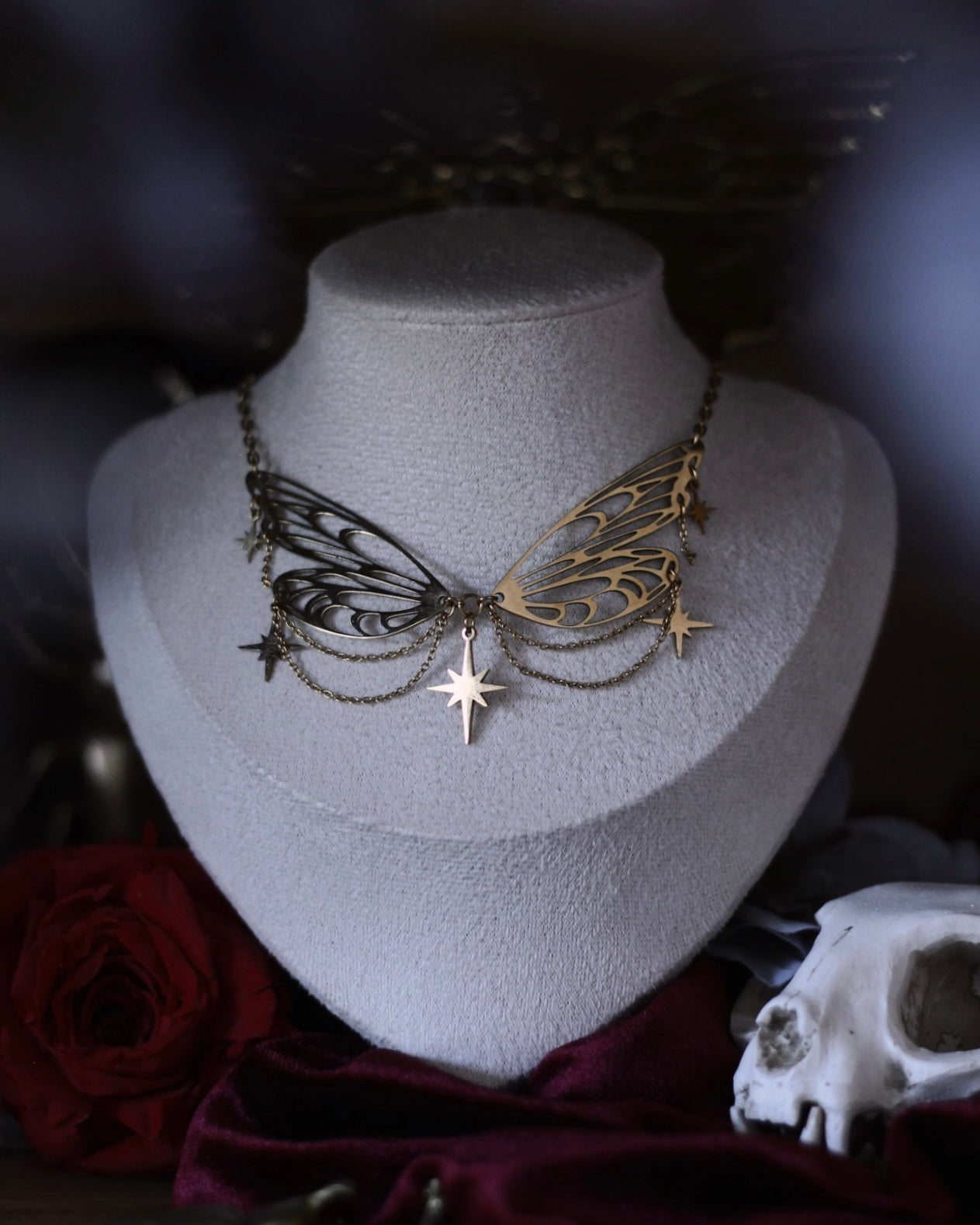 Collier Éos en acier inoxydable doré avec ailes ajourées, fines chaînettes et étoiles suspendues, porté en ras du cou.