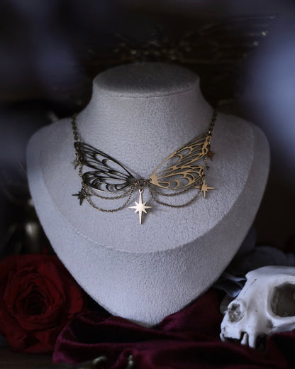 Collier Éos en acier inoxydable doré avec ailes ajourées, fines chaînettes et étoiles suspendues, porté en ras du cou.