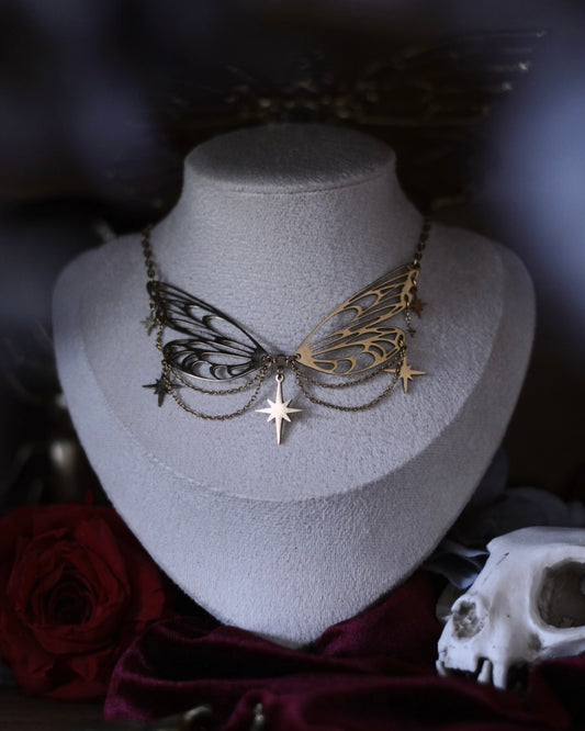 Collier Éos en acier inoxydable doré avec ailes ajourées, fines chaînettes et étoiles suspendues, porté en ras du cou.