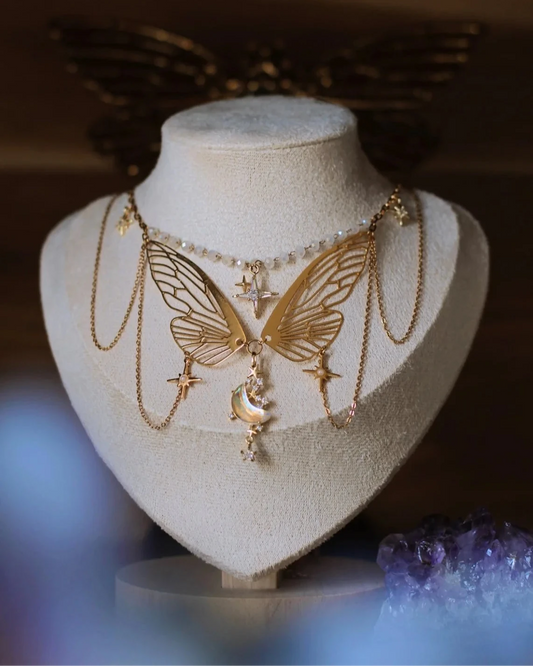 Collier doré "L’Éphémère Éternel" sur présentoir - ailes de papillon, lune irisée et étoiles
