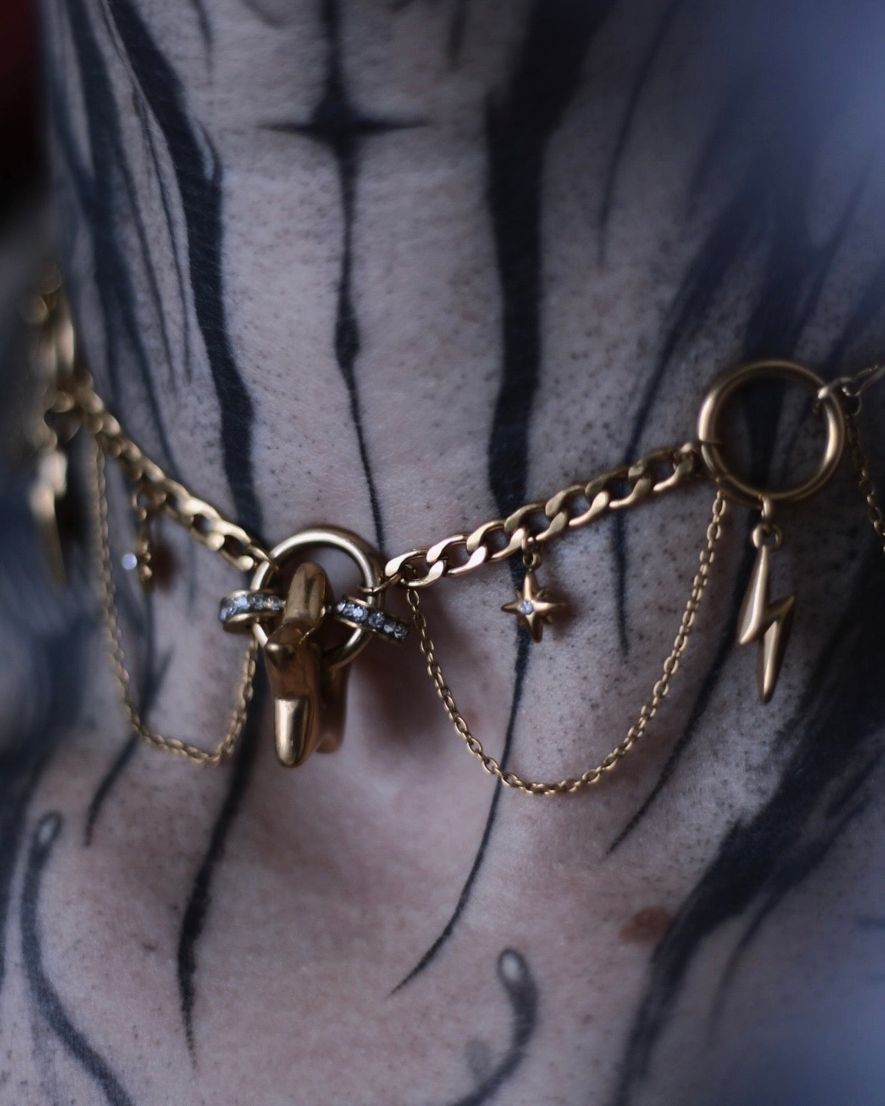 Collier Érèbe doré avec étoiles, éclairs et chaînes suspendues.