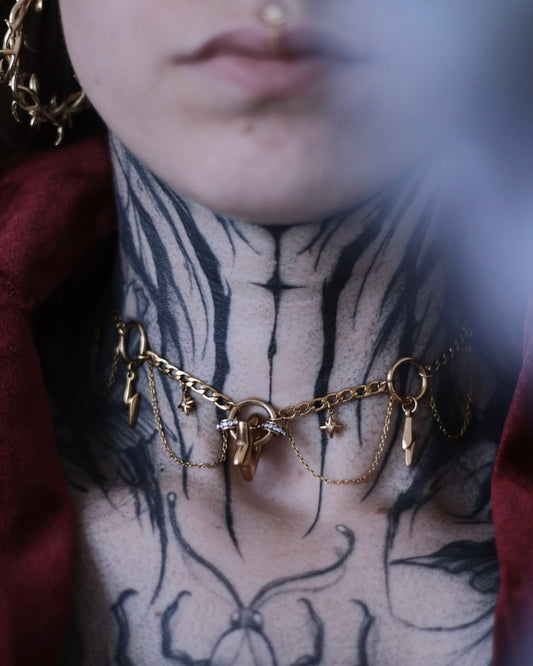 Collier Érèbe doré avec étoiles, éclairs et chaînes suspendues.