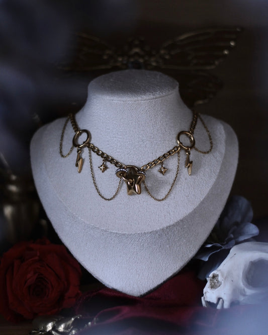Collier Érèbe doré avec étoiles, éclairs et chaînes suspendues.