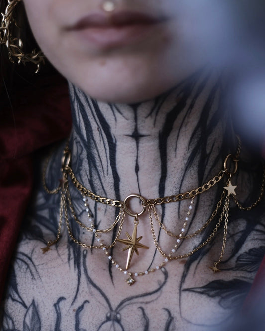 Collier L’Odyssée doré avec étoile centrale, chaînes suspendues et breloques étoilées