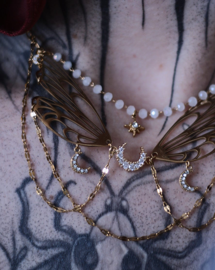 Collier Nova doré avec ailes ajourées, croissants de lune, étoile centrale et chaînes délicates.