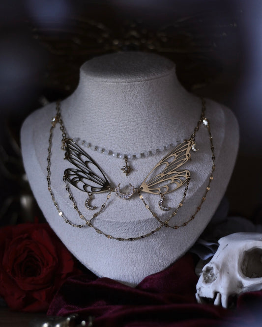 Collier Nova doré avec ailes ajourées, croissants de lune, étoile centrale et chaînes délicates.